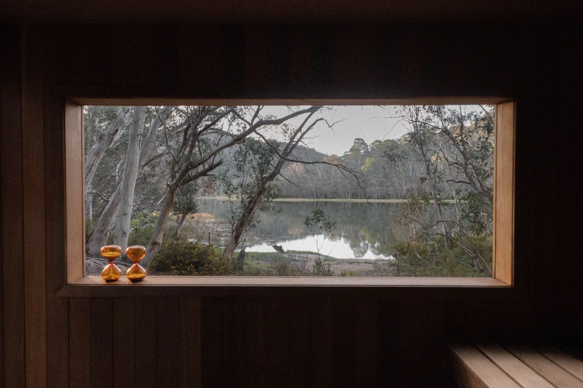 View from inside a lakeside sauna across a still bushland lake