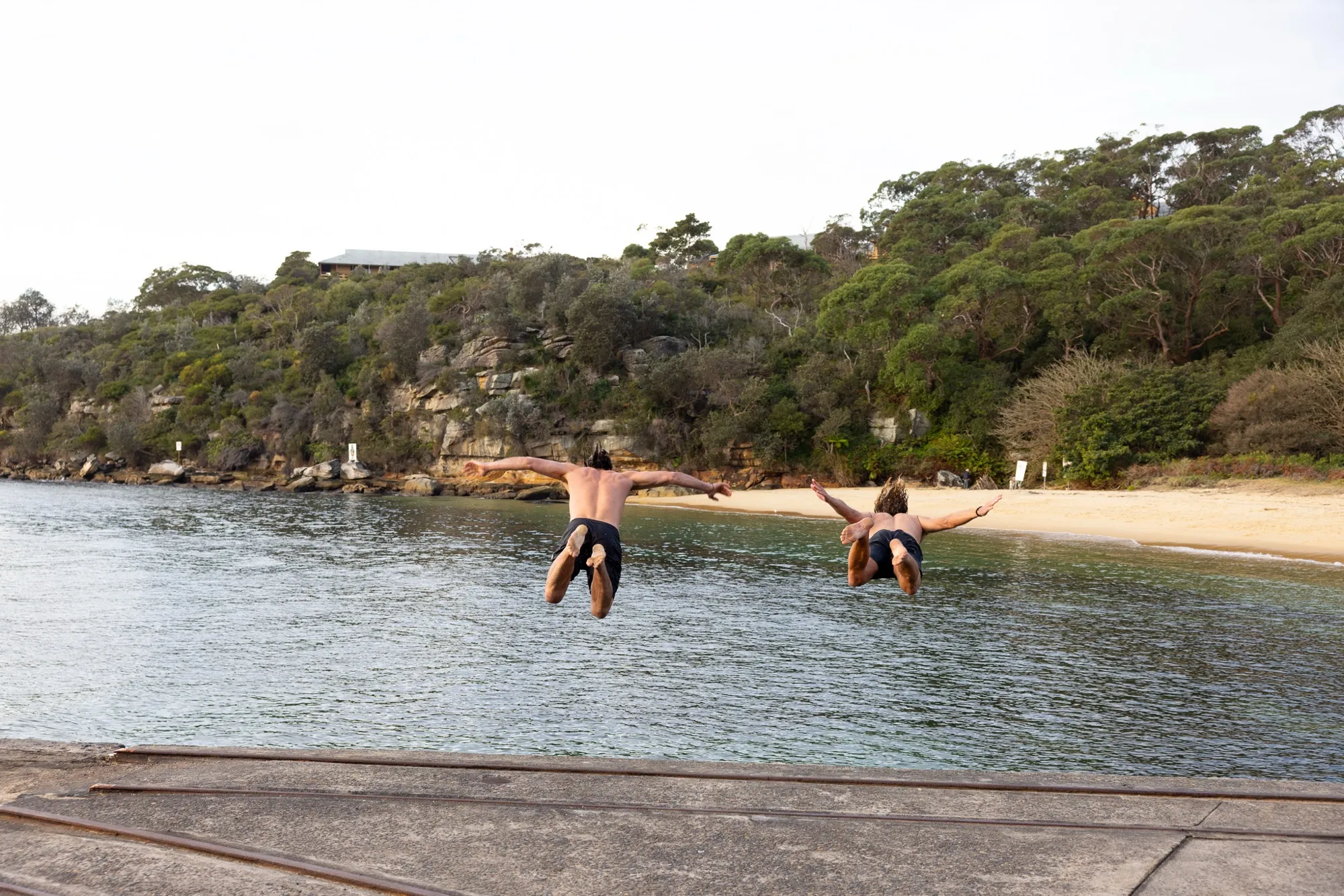 Two people leaping off a jetty into the bay at a sauna cove