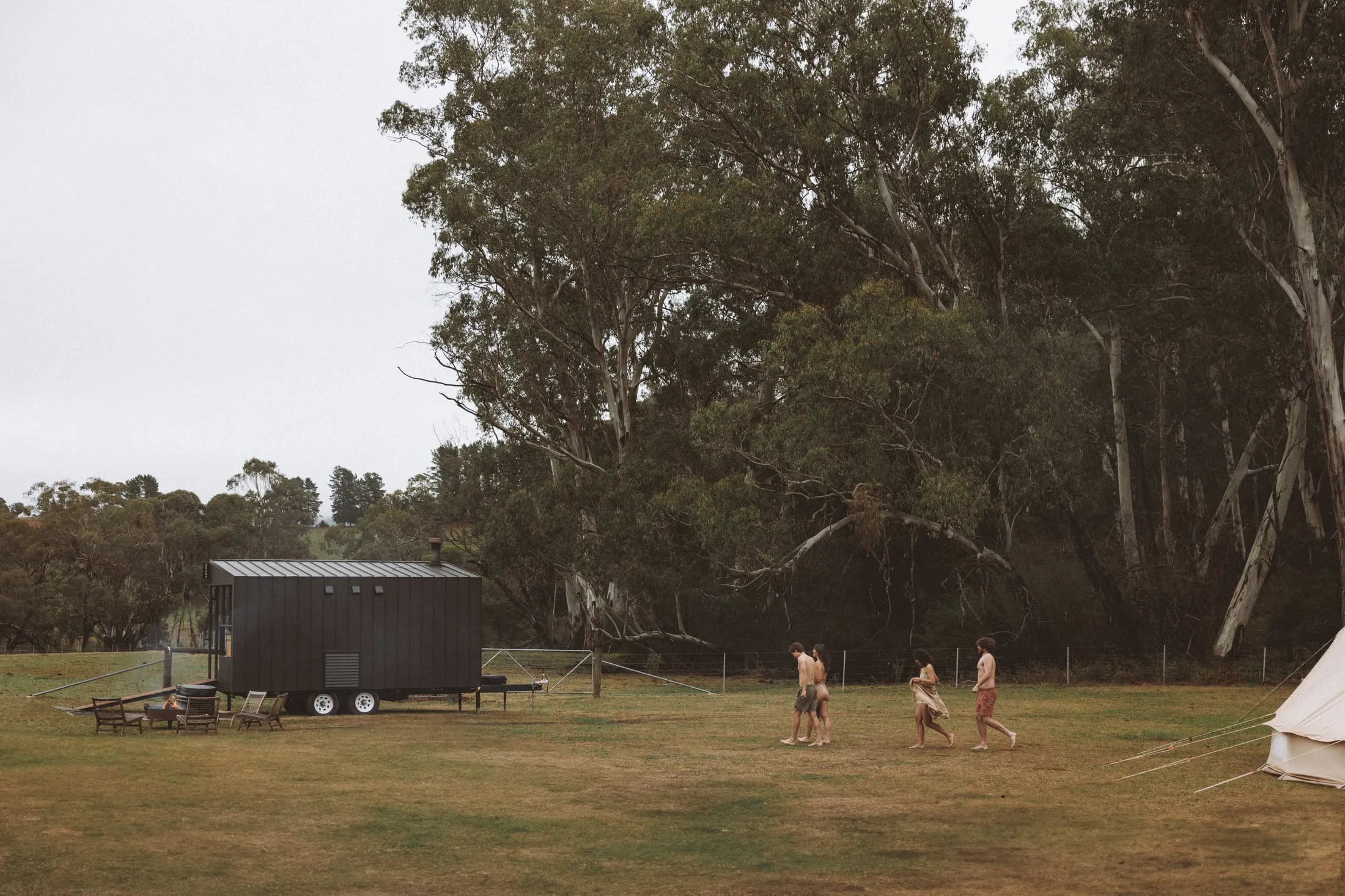 A wood-fired mobile sauna in the Australian bush, with people gathering nearby